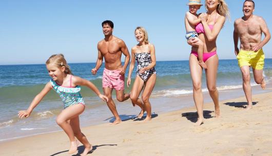Famiglia felice corre sulla spiaggia in una giornata di sole.