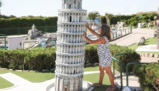 Bambina spinge la Torre di Pisa in miniatura in un parco.