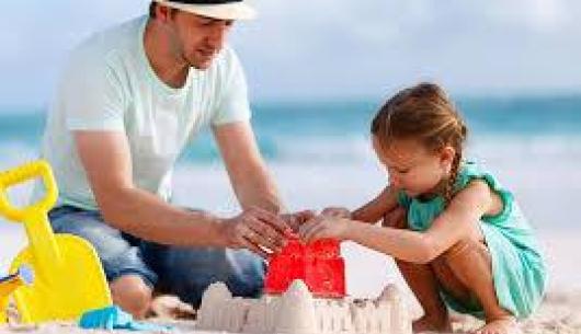 Uomo e bambina costruiscono castello di sabbia sulla spiaggia.