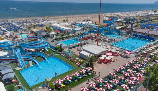 Parco acquatico con piscine, scivoli e spiaggia sul mare.