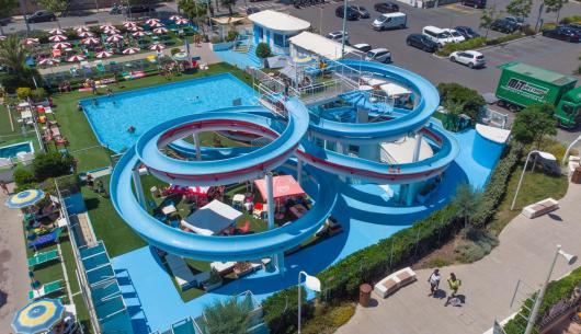 Parco acquatico con scivoli e piscina all'aperto, visitatori e ombrelloni colorati.