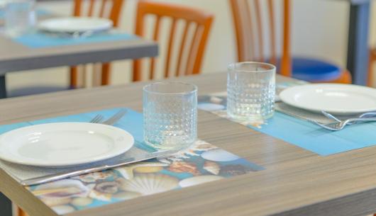 Tavola apparecchiata con piatti, bicchieri e posate su tovagliette blu.